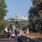 A pair of people walk towards a white city in the distance