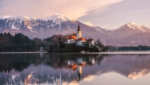 Alps in the background, buildings in midground, calm water in foreground