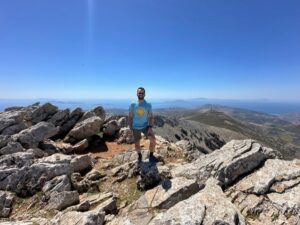 Boundless Journeys' guide Dimitri at the crest of a rocky hill, stopping for a sunny rest during our Greek hiking tour.